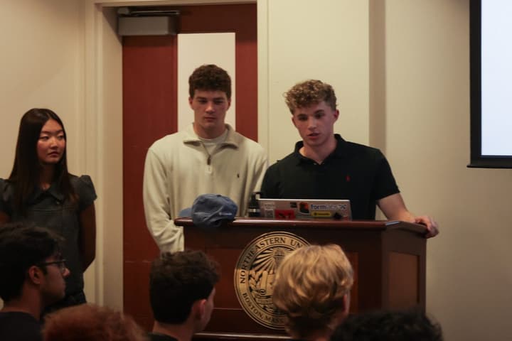 Three board members at the front of the room, one speaking from the podium.