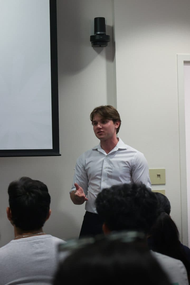 A board member presenting beside the screen, with the audience in the foreground.