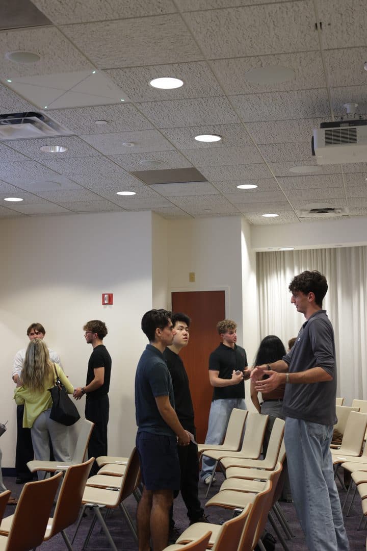 Students and board members talking in small groups as the room empties.